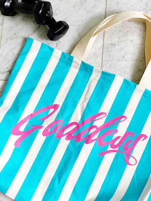 Our signature stripes luxe tote shown in a bold pink and blue with the word "Goddess" on the bag, features 2 interior pockets and a navy blue lining.